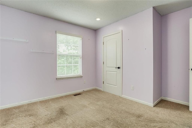 empty room featuring baseboards, carpet flooring, a textured ceiling, and visible vents