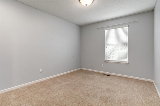 empty room with a textured ceiling, baseboards, light colored carpet, and visible vents