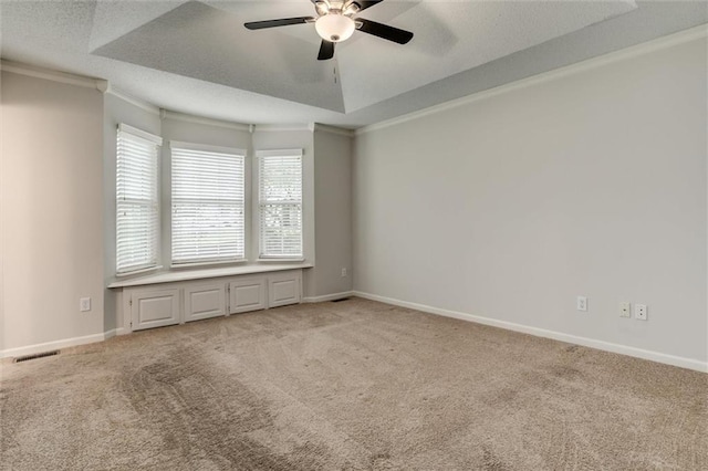 carpeted spare room featuring ceiling fan, a textured ceiling, baseboards, visible vents, and ornamental molding