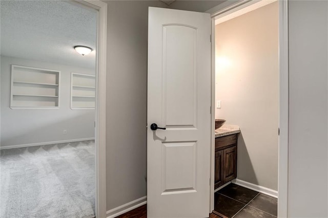 bathroom with baseboards, a textured ceiling, built in shelves, and vanity