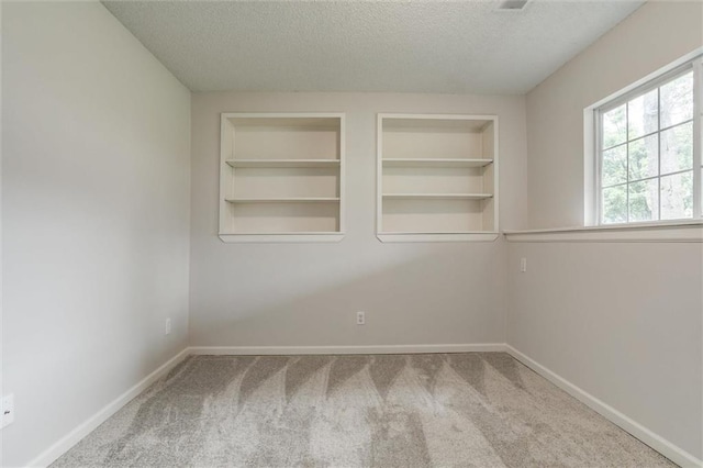 unfurnished room featuring a textured ceiling, built in shelves, baseboards, and carpet