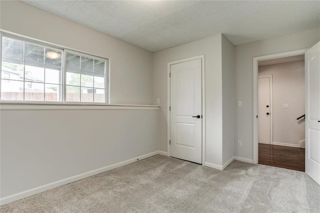 unfurnished bedroom with carpet floors, a textured ceiling, and baseboards