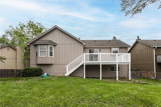 rear view of house featuring fence, a wooden deck, and a lawn