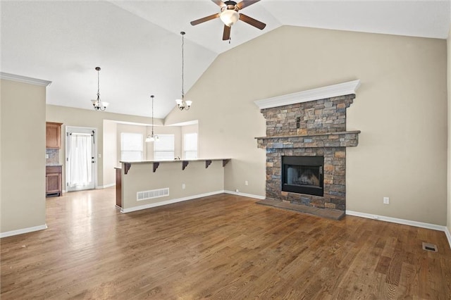 unfurnished living room with vaulted ceiling, visible vents, wood finished floors, a stone fireplace, and ceiling fan with notable chandelier
