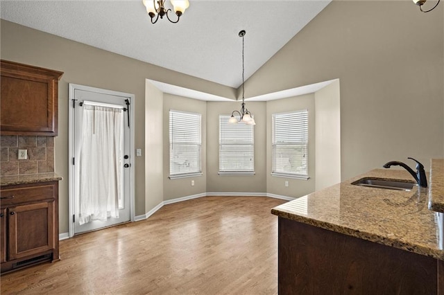 unfurnished dining area with a sink, light wood finished floors, baseboards, lofted ceiling, and a notable chandelier