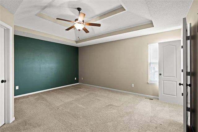 carpeted empty room featuring visible vents, a ceiling fan, baseboards, and a raised ceiling