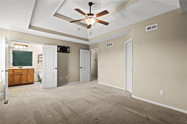 unfurnished bedroom with light colored carpet, baseboards, visible vents, and a raised ceiling