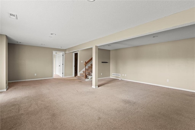 finished below grade area featuring baseboards, visible vents, carpet, and stairway