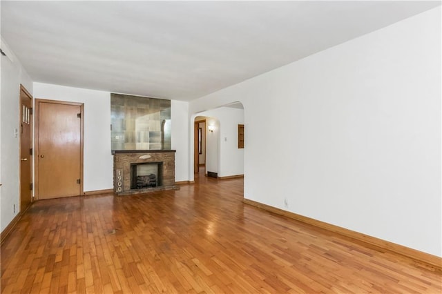 unfurnished living room featuring baseboards, arched walkways, light wood finished floors, and a fireplace with raised hearth