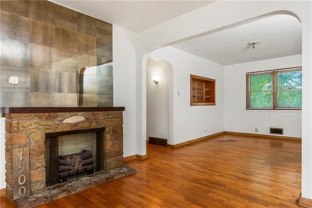 unfurnished living room with visible vents, wood finished floors, a fireplace, baseboards, and arched walkways