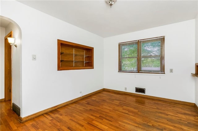 spare room featuring arched walkways, baseboards, and wood finished floors