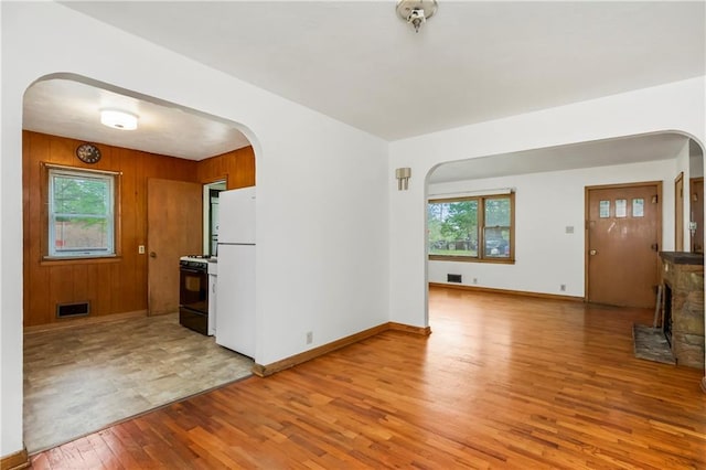kitchen featuring arched walkways, black gas range oven, freestanding refrigerator, and light wood finished floors
