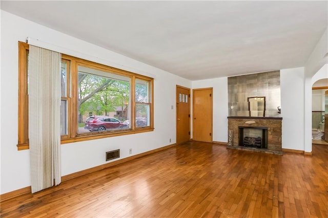 unfurnished living room featuring baseboards, arched walkways, hardwood / wood-style flooring, and a large fireplace