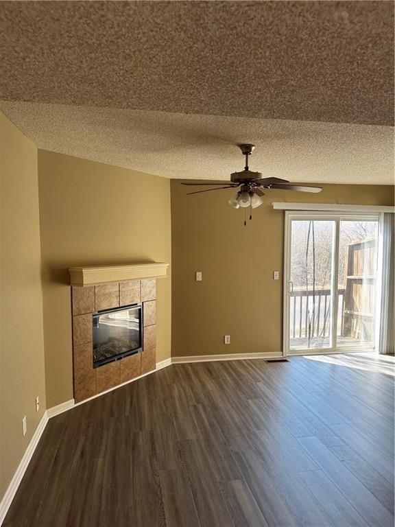 425 Hawthorne I Blvd, Warrensburg, MO 64093 - unfurnished living room with baseboards, dark wood finished floors, a textured ceiling, ceiling fan, and a tile fireplace