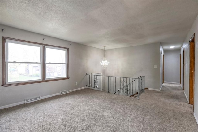 spare room featuring a textured ceiling, visible vents, carpet floors, and a chandelier
