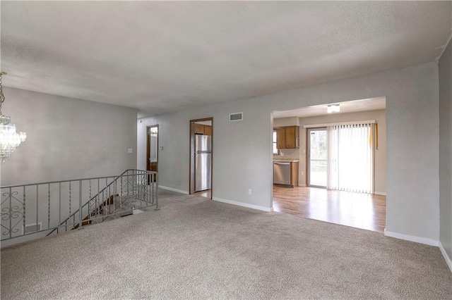 spare room featuring light carpet, a notable chandelier, visible vents, and baseboards