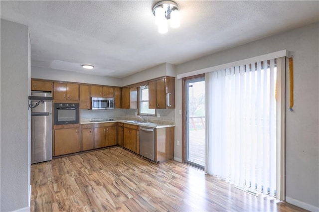 kitchen featuring light wood finished floors, brown cabinetry, light countertops, and black appliances