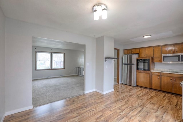 kitchen with light wood-type flooring, brown cabinetry, baseboards, and black appliances