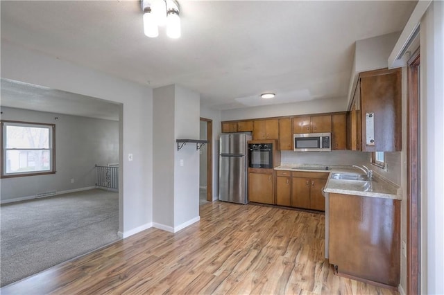 kitchen featuring brown cabinets, light countertops, a sink, light wood-style floors, and black appliances