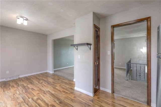 empty room featuring baseboards, wood finished floors, a textured ceiling, and visible vents