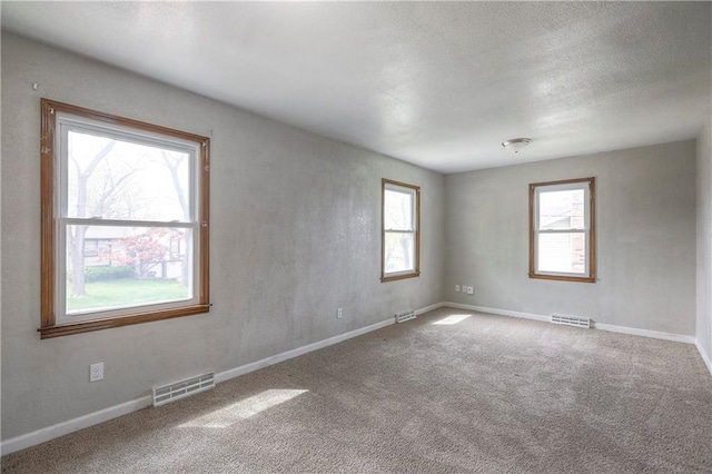 spare room featuring a textured ceiling, carpet floors, visible vents, and baseboards