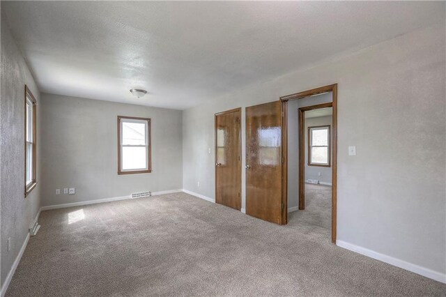carpeted spare room with baseboards, a healthy amount of sunlight, and visible vents