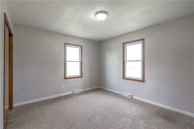 spare room with baseboards, carpet floors, visible vents, and a textured ceiling