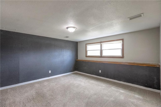 spare room featuring a textured ceiling, carpet flooring, baseboards, and visible vents