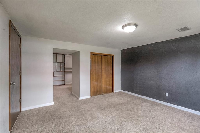 unfurnished bedroom with a textured ceiling, a closet, light carpet, baseboards, and visible vents