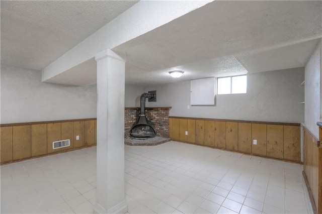 below grade area featuring wainscoting, wood walls, a textured ceiling, and visible vents