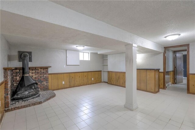 below grade area featuring wainscoting, a wood stove, a textured ceiling, and wooden walls