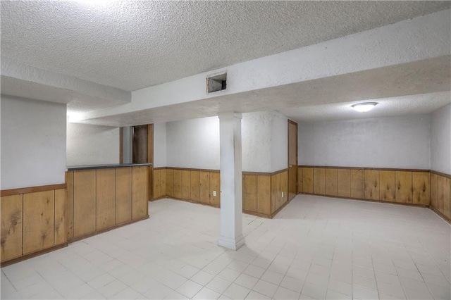 finished below grade area with a textured ceiling, a wainscoted wall, and wood walls