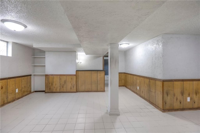 below grade area featuring a textured ceiling, wood walls, and wainscoting
