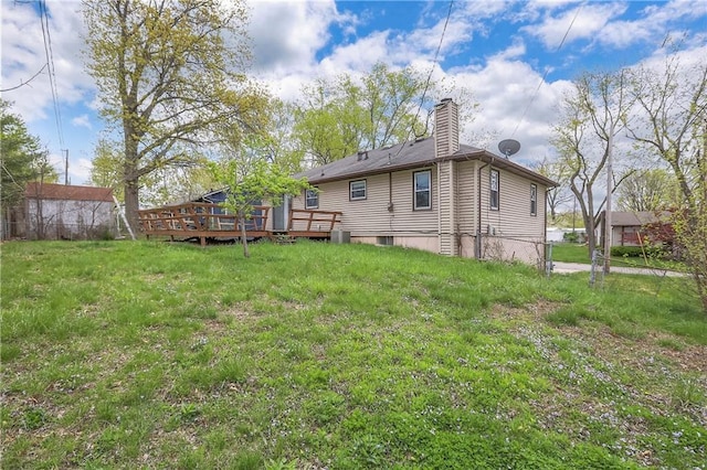 rear view of house featuring fence, a wooden deck, a chimney, and a yard