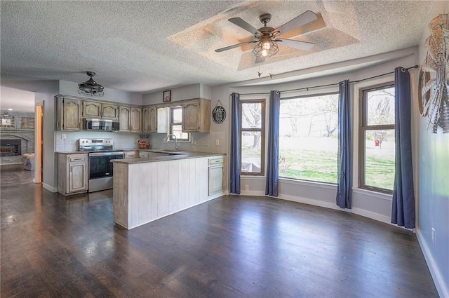 kitchen featuring a peninsula, appliances with stainless steel finishes, dark wood-style flooring, a sink, and baseboards