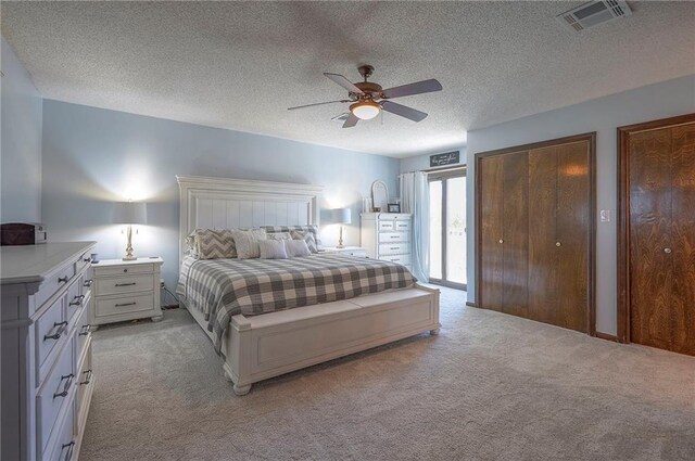 bedroom with a textured ceiling, light colored carpet, ceiling fan, and visible vents