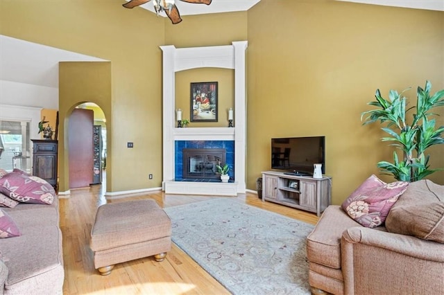 12848 S Rene St, Olathe, KS 66062 - living room featuring a ceiling fan, a tiled fireplace, arched walkways, wood finished floors, and baseboards