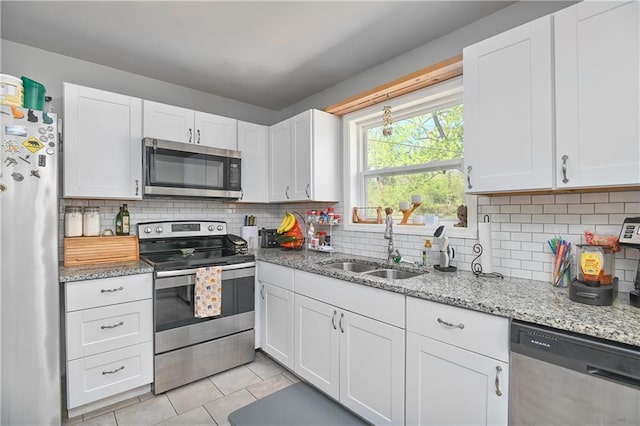 kitchen featuring light tile patterned floors, a sink, decorative backsplash, appliances with stainless steel finishes, and white cabinetry
