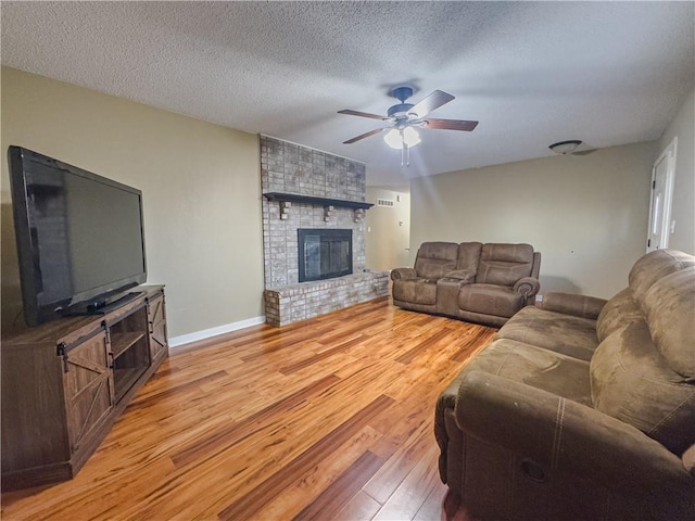 living area with baseboards, a fireplace, a textured ceiling, a ceiling fan, and light wood finished floors