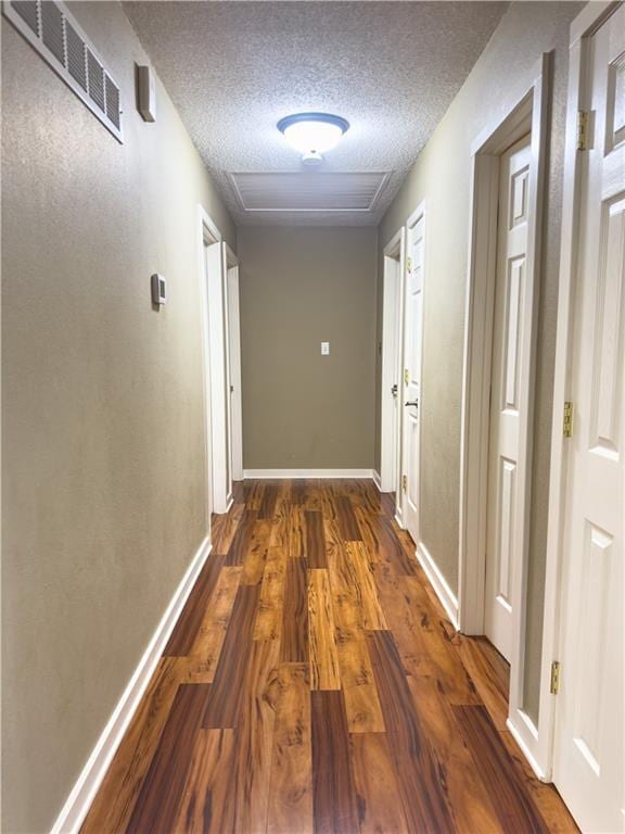 hallway with a textured ceiling, wood finished floors, baseboards, and visible vents
