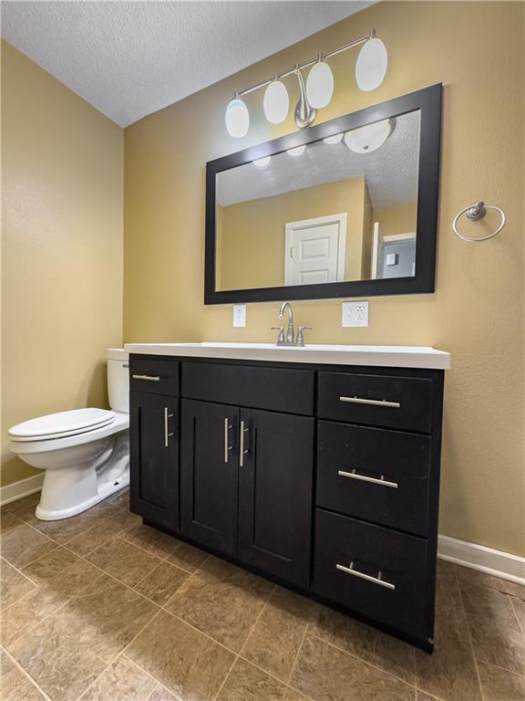 bathroom featuring vanity, baseboards, a textured ceiling, and toilet