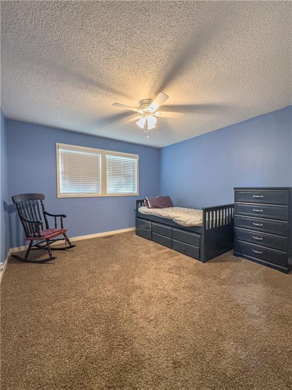 carpeted bedroom with a textured ceiling, baseboards, and a ceiling fan