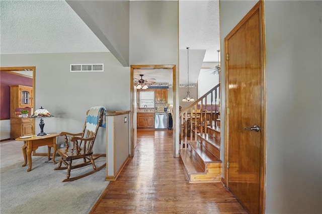 hall with baseboards, a textured ceiling, visible vents, and wood finished floors