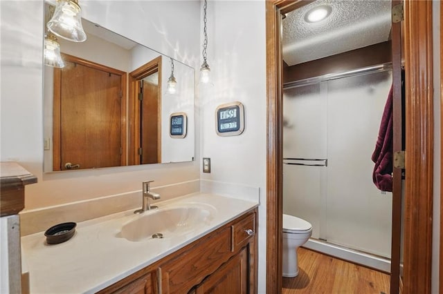 full bath with a textured ceiling, a shower stall, wood finished floors, vanity, and toilet