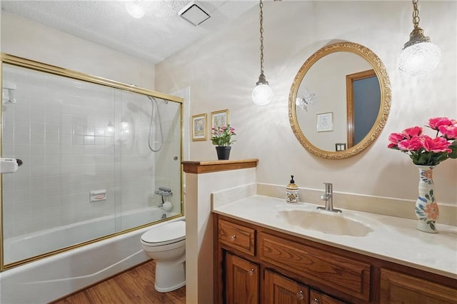 bathroom featuring vanity, wood finished floors, toilet, a textured ceiling, and combined bath / shower with glass door
