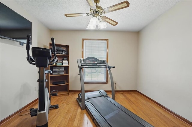 workout area featuring baseboards, a textured ceiling, light wood finished floors, and ceiling fan