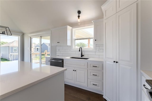 1308 N Holland Dr, Independence, MO 64056 - kitchen with a sink, stainless steel dishwasher, white cabinetry, decorative backsplash, and vaulted ceiling