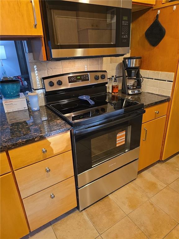 5101 NW Downing St, Blue Springs, MO 64015 - kitchen featuring stainless steel appliances, tasteful backsplash, light tile patterned floors, and dark stone counters