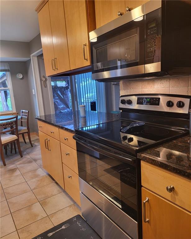 5101 NW Downing St, Blue Springs, MO 64015 - kitchen with stainless steel appliances, light tile patterned flooring, tasteful backsplash, and dark stone counters