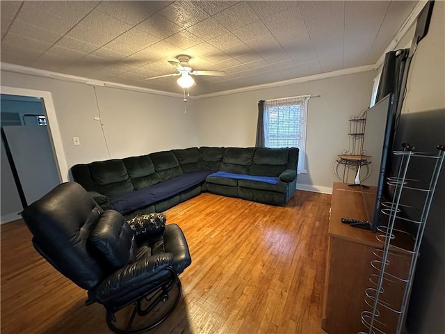 living area with baseboards, hardwood / wood-style flooring, ornamental molding, and ceiling fan